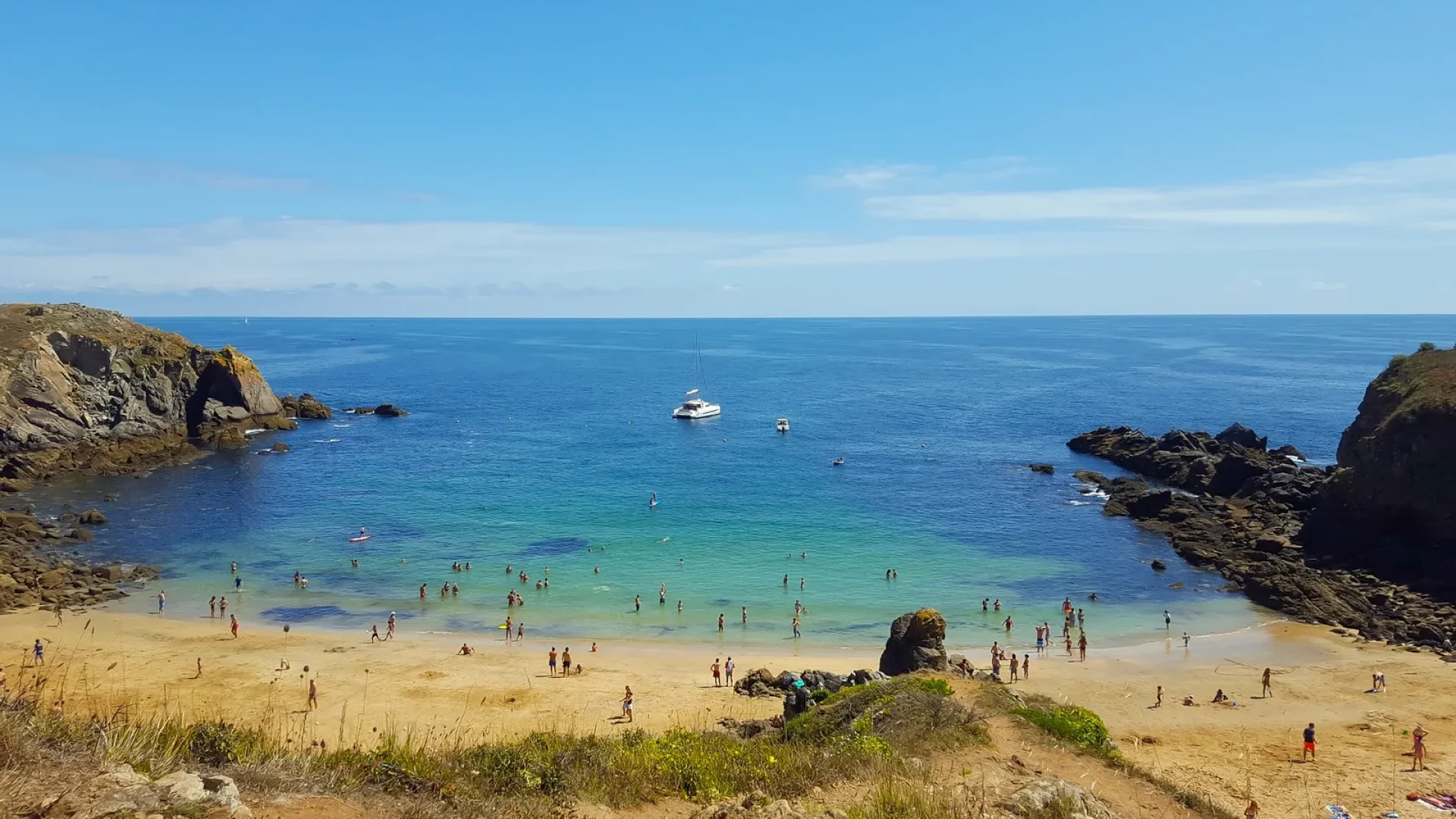 Photo of a beach on Ile d'Yeu, seen from a distance, with a boat on the sea and people on the sandy beach.