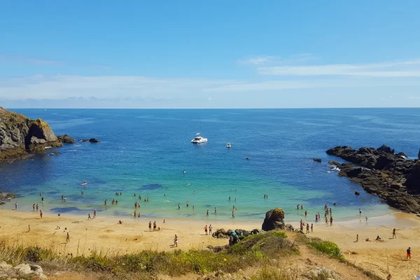 Photo of a beach on Ile d'Yeu, seen from a distance, with a boat on the sea and people on the sandy beach.